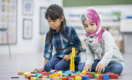 two young girls building a tower with toy blocks