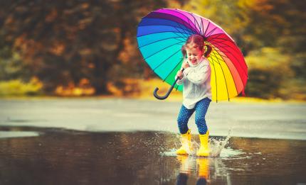 girl with umbrella jumping in a puddle