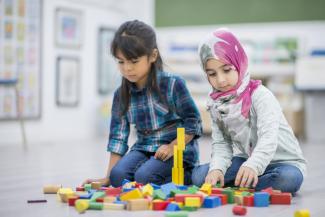 two young girls building a tower with toy blocks