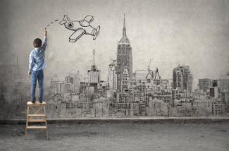 boy drawing a mural of a city